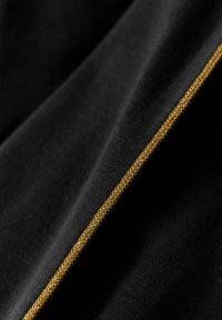 Svart tyg med en slät textur, prytt med en framträdande gyllene flätad kant längs kanten, vilket framhäver kontrasten i färg och design.