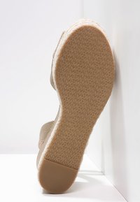 Suola di un sandalo con tacco a cuneo beige, con fondo in gomma testurizzata, sezione di presa del tallone visibile e dettagli in juta intrecciata lungo il plantare.