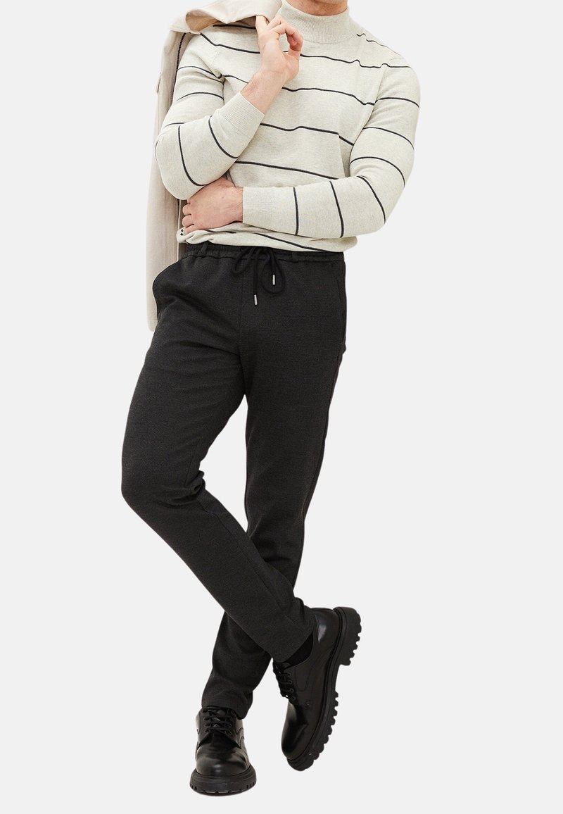 Světlé šedé pruhované svetrové triko s dlouhým rukávem, černé teplákové kalhoty s tahem na šňůrku a černé šněrovací boty s texturovanou podrážkou.