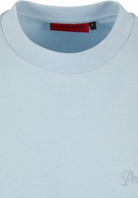 Camiseta de algodón azul claro con cuello redondo acanalado, sutil logo en la parte delantera y una etiqueta roja con "PROHIBIDO" en el interior del cuello.