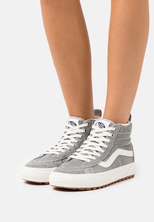 Zapatillas altas de ante gris, con cordones blancos y una distintiva franja blanca en el costado. Superficie texturizada y suela de goma.