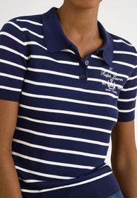 Námornícka modrá a bielo pruhovaná polo košeľa s golierom, krátkymi rukávmi, zapínaním na dva gombíky a vyšívaným logom na ľavej strane hrudníka.