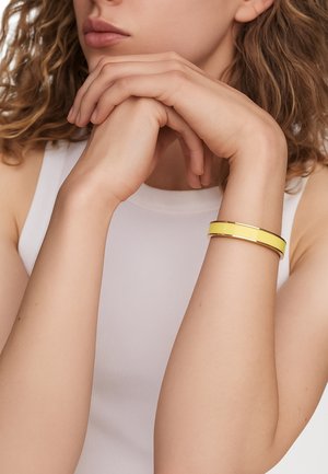 Yellow bangle bracelet with a shiny finish, featuring two parallel bands, worn on an arm against a plain white background.