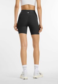 Mujer de pie de espaldas, vistiendo shorts de ciclista negros de cintura alta con relieve, sujetador deportivo blanco, calcetines blancos y zapatillas blancas.