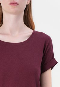 Burgundská krátka pánská blúzka s okrúhlym výstrihom, vyrobená z jemnej, textúrovanej tkaniny. Rukávy majú detail srolovaného lemu.