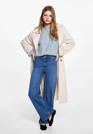 Beige Trenchcoat, hellblaue Hemdbluse, hochtaillierte blaue Schlagjeans, schwarze Schuhe. Das Outfit zeichnet sich durch eine lässige Passform und ein einfaches Design aus.