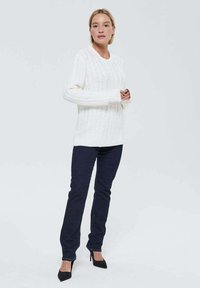 Sweater en tricot blanc avec un col rond et des manches longues, associé à un jean en denim foncé et des escarpins noirs. Texture lisse, coupe décontractée.