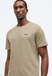 Μπεζ κοντομάνικο T-shirt με υφή υφάσματος, στρογγυλή λαιμόκοψη και διακριτικό μαύρο λογότυπο BOSS στο στήθος.