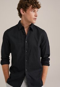 Črna srajca s dugimi rukavi, iz lahkega materiala, s klasičnim ovratnikom in sproščenim krojem ter gladko teksturo.