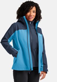 Veste imperméable bleue et marine avec fermeture éclair à l'avant, capuche et poches latérales. Présente une texture lisse et un design à blocs de couleur.