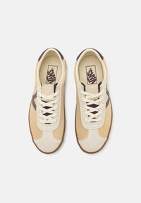 Chaussures de sport en suède beige et cuir crème avec des accents marron, dotées de lacets blancs et d'un détail de couture en zigzag le long de la languette.