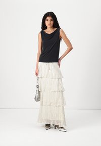  Haut sans manches noir avec un décolleté drapé, associé à une jupe blanche à volants ornée de pois noirs, accessoirisé avec un sac à main argenté.