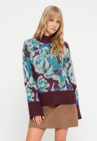 Maglione lavorato a maglia con un motivo floreale multicolore nelle tonalità di verde, blu e borgogna; presenta un collo alto e maniche larghe, texture morbida.