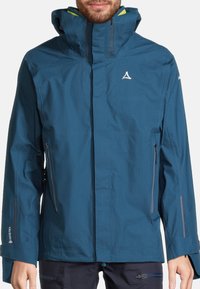 Giacca blu impermeabile da uomo con finitura testurizzata, cappuccio regolabile, zip frontale e tasche laterali. Presenta un logo sul petto e sulle maniche.