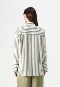 Striped lightweight jacket with a textured cream fabric and narrow black stripes. Features long sleeves and a straight cut, with a back yoke.