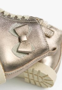 Metallic gold Schuhe mit strukturiertem Finish, versehen mit einer dekorativen Schleifenakzent und einer hellen Gummisohle.
