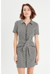Robe à manches courtes noire et blanche avec un motif, un col, une fermeture éclair à l'avant et un détail de taille nouée. Comprend deux poches zippées.