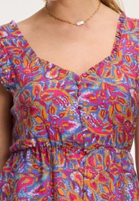 Krāsains zieds drēbes, kas ir ar V veida dekoltē, viļņotām piedurknēm un pogām priekšpusē. Audums ir ar teksturētu, vieglu dizainu.