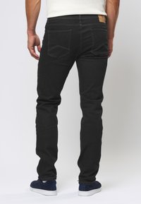 Zwarte denim jeans met een slim fit, met twee achterzakken en een leren label op de tailleband. Gecombineerd met blauwe sneakers.