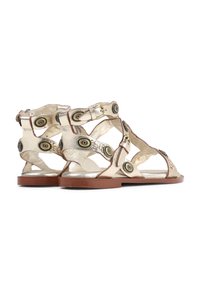 Gouden metallic sandalen met uitsnijdingen, contrasterende bruine zool, decoratieve cirkelvormige hardwareaccenten op de banden en een gladde textuur.