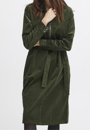 Robe en velours côtelé vert avec ceinture, manches longues, fermeture éclair à l'avant et col. Le tissu présente un motif côtelé texturé.