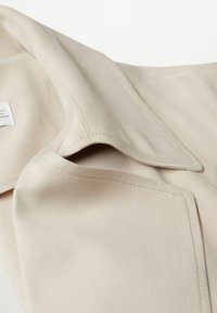 Gros plan sur un tissu beige avec des coutures visibles et des ourlets repliés, mettant en avant la texture et les détails de construction du vêtement.