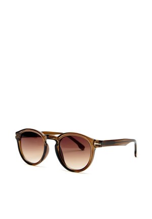 Lunettes de soleil rondes transparentes marron avec verres dégradés foncés posées sur une surface blanche, inclinées vers la droite.