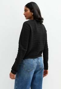 Un pull noir texturé avec des manches longues et un design court, associé à un jean en denim bleu taille haute.