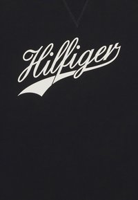 Sudadera negra con un logo cursivo blanco "Hilfiger" en el pecho, de diseño en pico y tela texturizada.