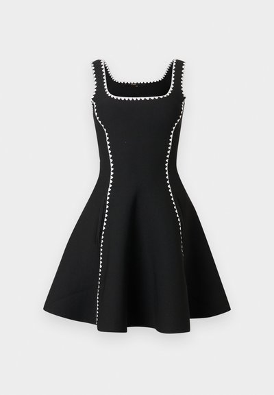 Robe noire sans manches en ligne A avec encolure carrée, ornée d'un biais zigzag blanc le long de l'encolure, des côtés et des bretelles.