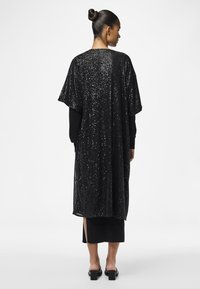 Kaftan lung negru cu paiete, cu mâneci scurte, fante laterale și un strat interior neted, conceput pentru o croială lejeră și o cădere elegantă.