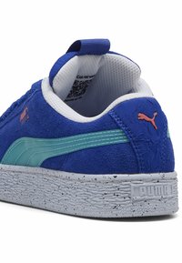Plave antilop teniske cipele s tirkiznim akcentnim trakama, teksturiranim potplatom, belim točkastim đonom i plavim petnim trakama. Puma logo u narančastoj boji.