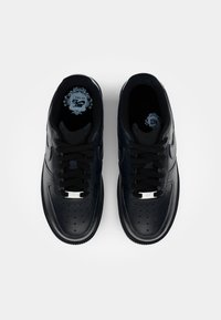 Svarta lädersneakers med perforerat tåbox, plana svarta snören och silverdetaljer på tungan. Texturerad sula med en slät yta.