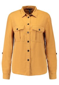 Senapsgul skjorta med knäppning fram, två bröstfickor och långa ärmar med justerbara manschetter. Tillverkad av ett mjukt tyg.