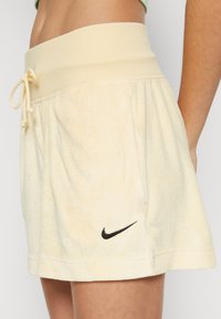 Krátké, světle žluté šortky z měkké látky. Mají široký elastický pas, šňůrkové zavazování a malý černý logo Nike.