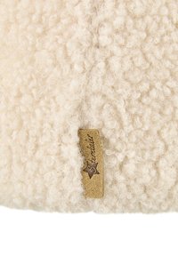 Cream-colored textured wool fabric with a small tan suede tag featuring a dark star and cursive brand name.