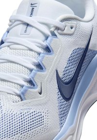 Zapatilla deportiva de Nike con una parte superior de malla blanca, acentos en azul claro y un logotipo de swoosh en azul oscuro. Presenta cordones planos y una suela texturizada.