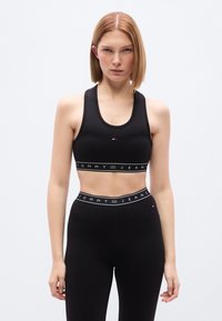 Μαύρο αθλητικό σου τιέν και κολάν με ψηλή μέση, κατασκευασμένα από λείο ύφασμα με ελαστικές ζώνες που φέρουν το λογότυπο «TOMMY JEANS» σε λευκό.