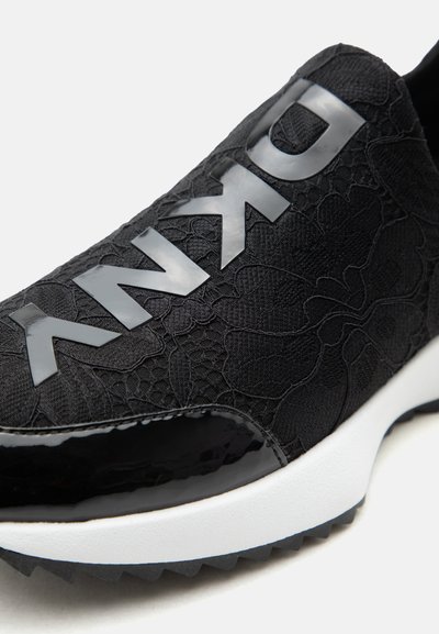 Baskets noires avec logo ANNA en relief sur le dessus, dessus en tissu fleuri texturé, bout noir brillant et semelle blanche.