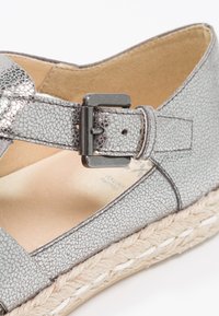 Espadrille argenté métallique avec tige texturée et boucle réglable. Comprend une semelle en jute tissé pour ajouter de la texture et du contraste.
