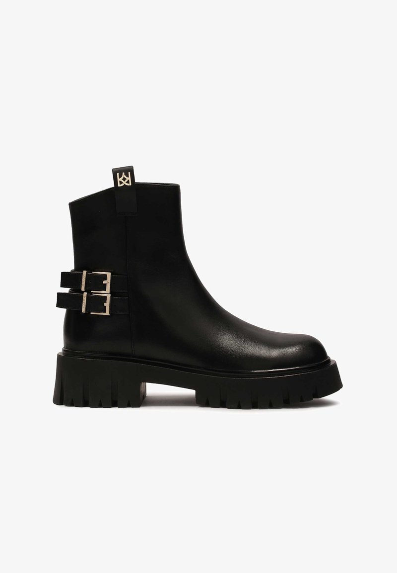 Černá kotníková kožená bota s masivní platformovou podrážkou, dvojitými přezkami na straně a poutkem vzadu. Hladká textura a elegantní design.