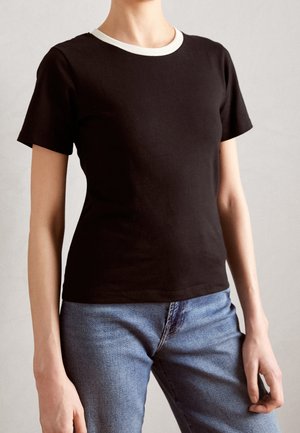 Sort bomulds t-shirt med kontrast hvid rund hals, korte ærmer og tætsiddende design, parret med lyseblå jeans.