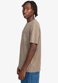 Koszulka z krótkim rękawem w kolorze oliwkowym, wykonana z bawełny, z kieszonką na piersi i luźnym krojem. Teksturowana tkanina z widocznymi detalami szwów.