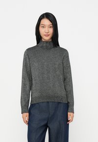 Suéter cinza de gola alta com um brilho metálico subtil, mangas longas e um corte descontraído, combinado com calças azul-escuro.