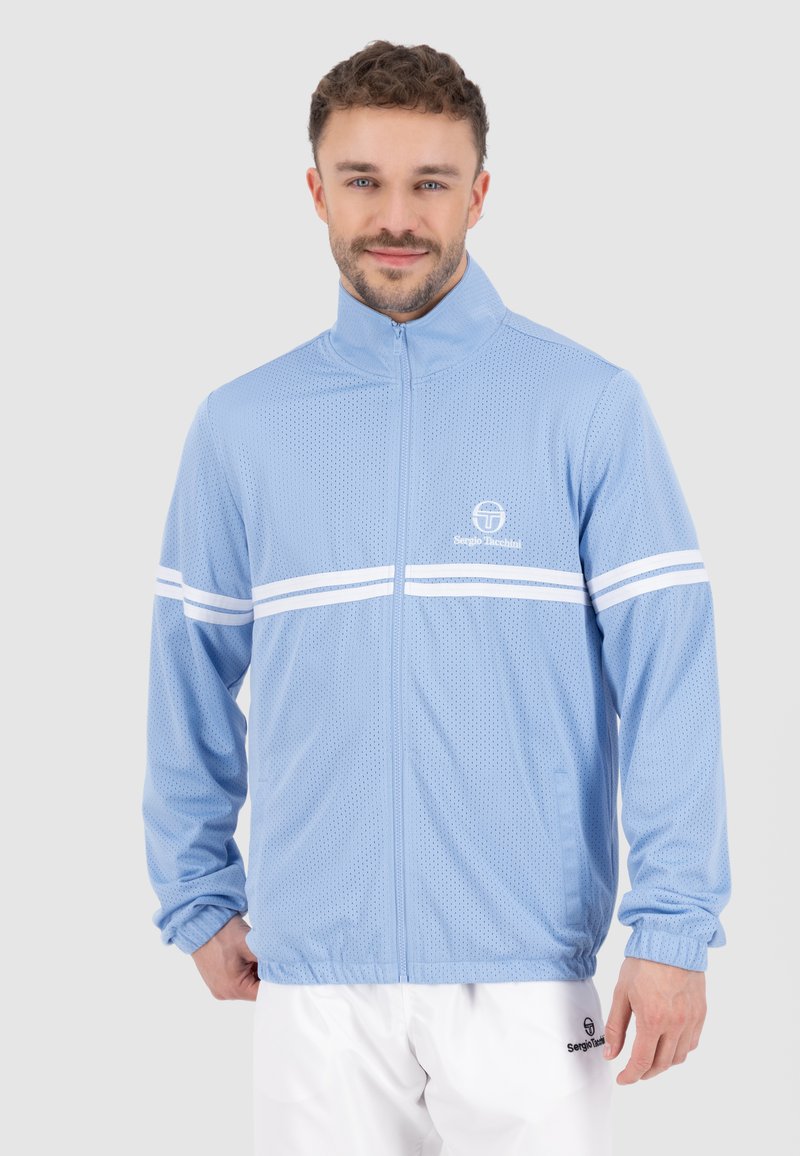 Giacca a rete blu chiaro con strisce orizzontali bianche, chiusura con zip davanti, colletto alto e polsini elastici. Presenta il logo sul lato sinistro del petto.
