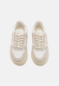 Sneakers beige e bianchi presentano una punta perforata, dettagli in suede e lacci texturizzati, con un logo discreto sul lato.