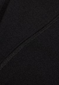 Svart tyg med en slät yta har kontrasterande sömmar och subtila sömnadsdetaljer. Materialet har en lätt stretch och flexibilitet.