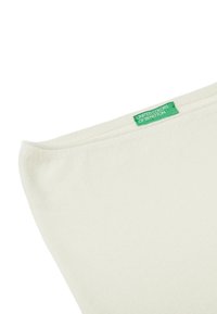 Textilie krémové barvy s hladkou texturou, na jejíž horní hraně se nachází malý zelený štítek s nápisem "United Colors of Benetton".