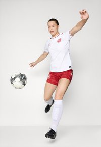 Valge jalgpallipait, millel on punased aktsendid, punased lühikesed püksid, mustad tossud ja valged sokid, löömas musta ja valget jalgpall.