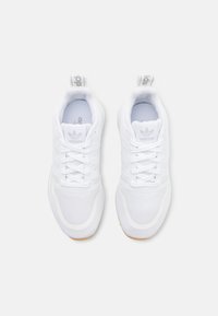 Zapatos deportivos blancos con parte superior de malla, que cuentan con acentos de tres rayas, puntera redonda y suela de goma texturizada. Incluye una lengüeta en el talón.